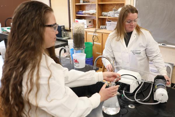 Two women inserting a tube in a glass beaker